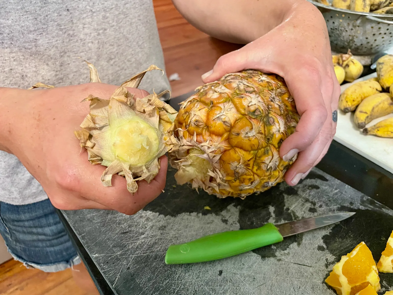 Hands twisting the leafy crown off a harvested pineapple.